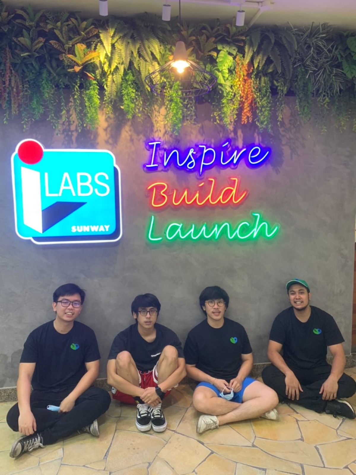 A full portrait shot of SpargoEats’ team of four comprising four males – all wearing their signature black tee shirt, seated on the floor beneath Sunway iLabs LED sign board, led by co-founder and CEO Nicholas Ou.