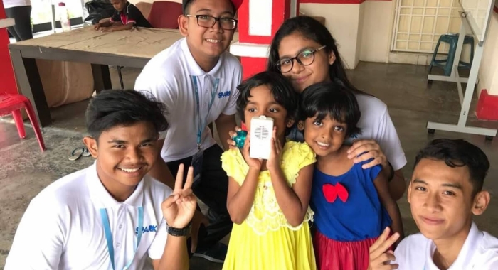 A medium landscape shot of Harvynna Kaur Kler smiling demurely alongside school mates and child beneficiaries during a charitable school project