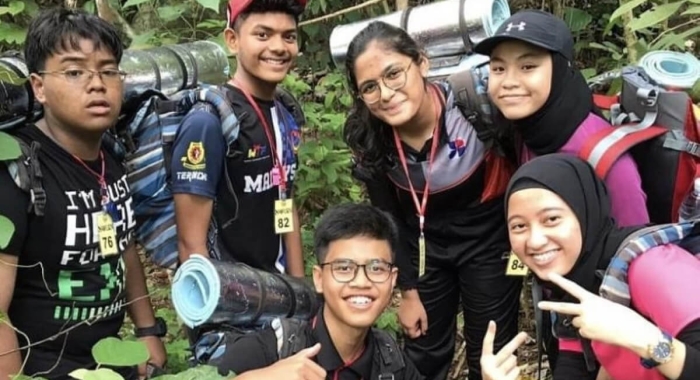 A medium landscape shot of Harvynna Kaur Kler smiling demurely among peers on a hiking trail