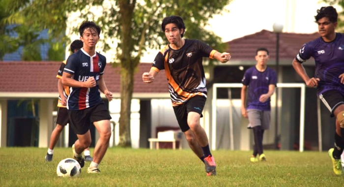 A full landscape shot of Muhammad Luqman Mohammad Nawar in hot pursuitamidst a football tournament