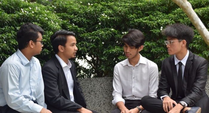 A medium landscape shot of Muhammad Luqman Mohammad Nawar dressed in a white button-up and black slacks, sitting between similarly dressed-up companions