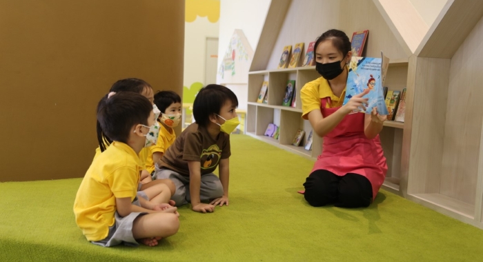 A full landscape shot of a Sunway Little Sunshine homeroom teacher reading aloud to toddlers by the centre’s designated Reading Tree