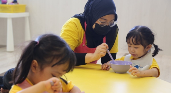 A loose close up shot of a Sunway Little Sunshine homeroom teacher feeding a toddler during mealtime