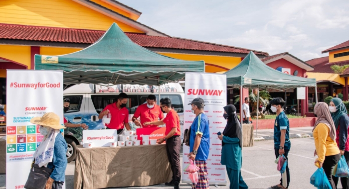 A full landscape shot of Sunwayians donning signature red polo tees distributing bubur lambuk to local communities as part of our #SunwayforGood Raya Cheer 2022 at Dataran Lenggong, Perak