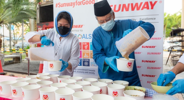 A medium full landscape shot of Sunway Group deputy chairman Tan Sri Datuk Seri Razman M. Hashim alongside Sunway Group Brand Marketing and Communications senior general manager Nik Tasha Nik Kamaruddin dispensing bubur lambuk to B40 communities at Masjid Al-Husna in Selangor.