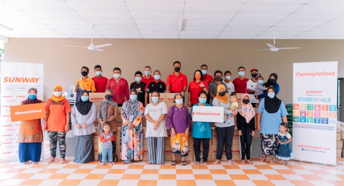 A full landscape shot of the Orang Asal community in Kampung Sg. Choh alongside Sunwayians donning signature red polo tees in the town’s multi-purpose hall after groceries and essential goods distribution