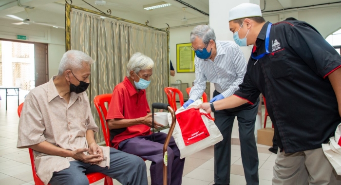 Tan Sri Razman handing the B40 a bag with essential items, alongside another man clad in black shirt.