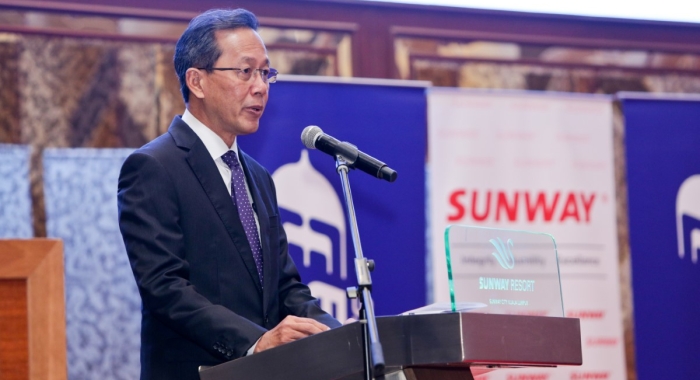 A medium landscape shot of Malaysian Aviation Group chief executive officer Captain Izham Ismail giving a speech on-stage behind a Sunway Resort Hotel podium.