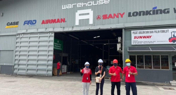 Sunway staff wearing hard hats at a Sunway warehouse, posing with thumbs up for the camera.