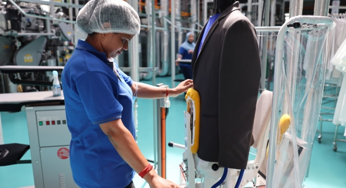 A medium full landscape shot of a Sunway Pristine Laundry staff carefully steaming and pressing a blazer suit using a Sankosha industrial steamer.