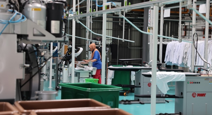 A full landscape shot of the Sunway Pristine Laundry plant garment section featuring a staff ironing clothing using a Sankosha industrial steam press as the focal point.