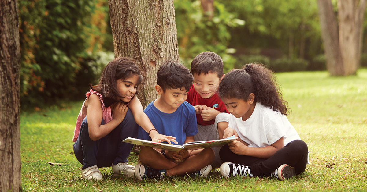 A group of children reading a book in a green field